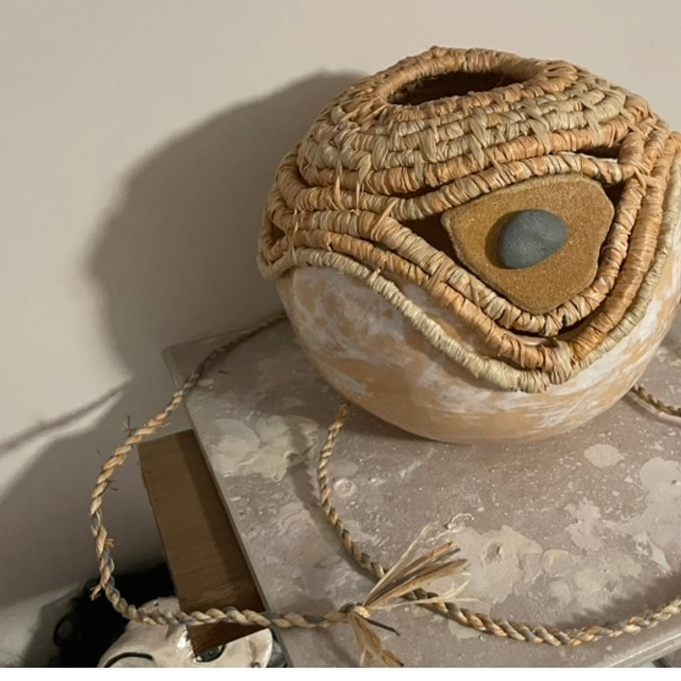 Round coiled vessel with a smooth river stone set into the fibre, on a plinth