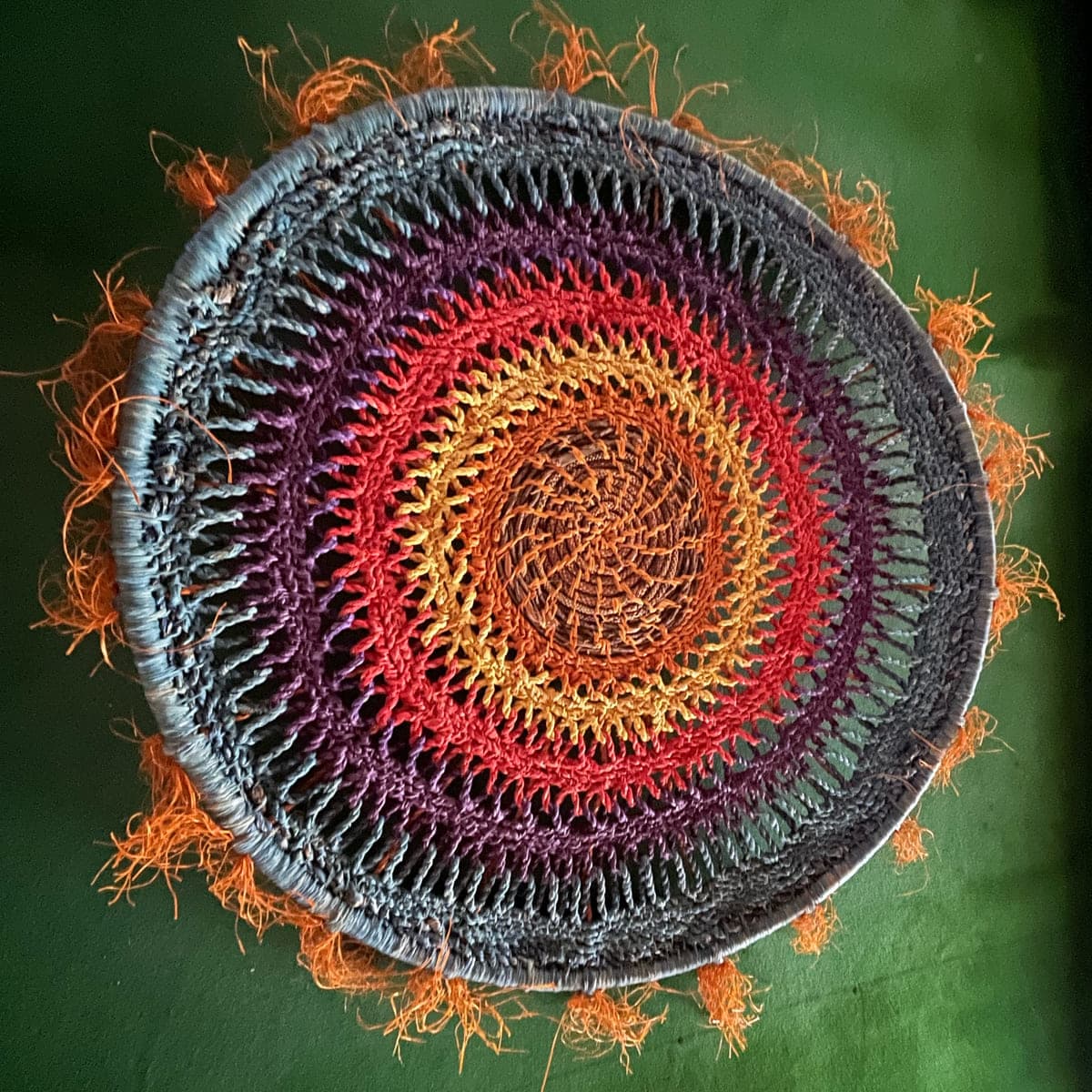 A circular coiled mandala in red, orange and grey